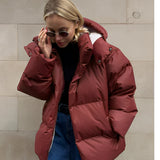 
A woman wearing a stylish oversized blue hooded puffer jacket with a mahogany color lining, featuring long sleeves and a waist-length design, accessorized with sunglasses.