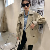 
A woman standing confidently wearing an oversized double-breasted black blazer, styled with a white dress shirt underneath. She is accessorized with chic sunglasses and is dressed in fashionable outerwear.