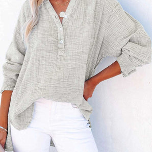 Woman wearing a light gray oversized linen V-neck blouse, lightweight and breathable, buttoned up, with a 2XL fit, standing and showing shoulder and sleeve details.