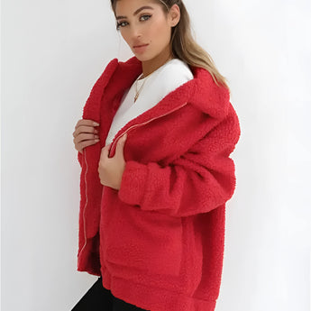 
A woman wearing an oversized red teddy coat with long sleeves and a plush texture, suitable for winter. The coat is designed with a wide collar and falls to the waist, creating a stylish and cozy look. The model showcases the coat in a fashion setting.