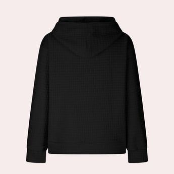 
A woman wearing an oversized textured black hoodie with a casual loose fit, featuring long sleeves and a comfortable collar.