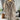 Woman wearing a beige oversized wool hooded sweater coat, displayed on a clothes hanger, with a cozy winter design. The coat is hanging in a room decorated with potted plants and houseplants in the background. The sweater features a collar and long sleeves.