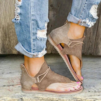 Brown peep-toe wraparound ankle sandals in an earth tone bohemian style, worn by a person pairing them with denim jeans, showcasing the shoe's flat sole and stylish design.