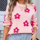 Women's pink floral crewneck sweater worn by a model. The sweater features a trendy autumn knitwear design with floral patterns. The model is accessorized with sunglasses and has shoulder-length hair, showcasing the sweater's stylish appearance.