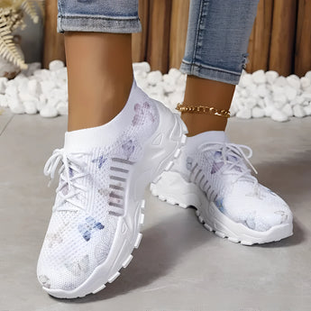 Women's pink floral mesh running shoes with white soles, worn by a person dressed in grey denim sportswear.