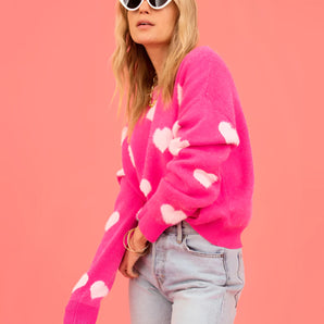 Pink heart-patterned fuzzy knit cardigan worn by a woman, paired with jeans and sunglasses, showcasing a trendy and cozy fashion statement.