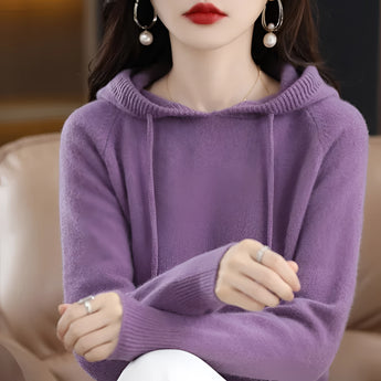 
A woman wearing a soft knit women's hooded sweater in pink, sized 2XL, featuring a cozy winter design. The sweater is styled with a hood, and the color is identified as Viola, a shade of purple. The woman is visible from the shoulders up, highlighting the sweater's texture and style.