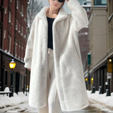 Women's oversized teddy coat in pink, featuring a plush and furry texture. The coat has a design that includes a defined waist and long sleeves. It is styled for winter fashion and is displayed against a snowy background.