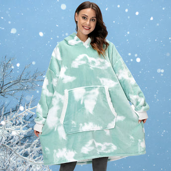 
A woman smiling and standing outdoors wearing a green plush oversized fleece hooded robe, designed for warmth and comfort in winter. The robe features long sleeves and a cozy fit, suitable as loungewear. Nature and trees are visible in the background, enhancing the serene and happy mood.