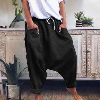 A pair of women's black bohemian harem pants with an elastic ankle and drawstring waist, shown in size XL. The pants are displayed alongside a houseplant in a white flowerpot.