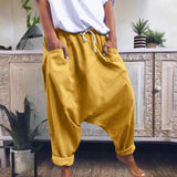 A pair of women's red bohemian harem pants, featuring an elastic ankle and drawstring waist, laid on a wooden floor with a yellow decorative element nearby.