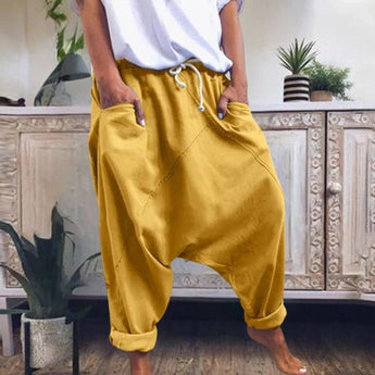 A pair of women's red bohemian harem pants, featuring an elastic ankle and drawstring waist, laid on a wooden floor with a yellow decorative element nearby.