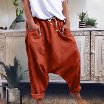 A pair of women's red bohemian harem pants with elastic ankles and a drawstring waist, displayed in an orange color in size XL, against a backdrop featuring houseplants and flowerpots.