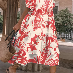 
A woman wearing a red floral midi dress with a V-neck design, suitable for casual beachwear. The dress features short sleeves and falls below the knee, showcasing a vibrant red and pink floral pattern. The image highlights the dress being worn outdoors, capturing a fashionable and relaxed style.