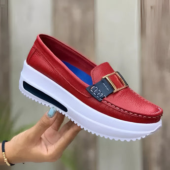 Women's red leather platform loafers with fashion buckle detail, shown on a foot.