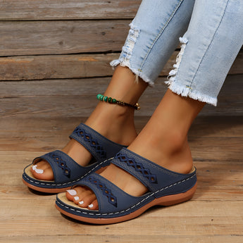 Dark blue leather platform sandals worn on a woman's foot, styled with denim and a blazer, showcasing a fashionable summer look.