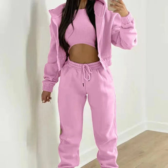 Women's pink tracksuit consisting of a cropped puffer jacket and drawstring joggers, worn by a model standing with arms slightly bent, showcasing the outerwear with sleeves and active pants, highlighting the fit around the waist and neck.