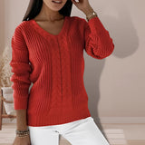 A woman wearing a sage green V-neck cable knit chunky sweater, showcasing the textured design on the sleeves and body, with a relaxed and cozy fit.