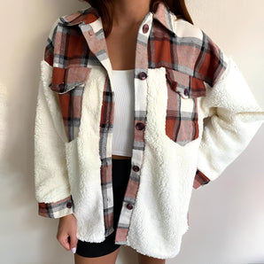 Women's brown sherpa-lined plaid flannel jacket in XL, featuring a cozy winter shacket style with tartan pattern. The jacket is designed for warmth and comfort, showcasing details such as a collar and long sleeves.