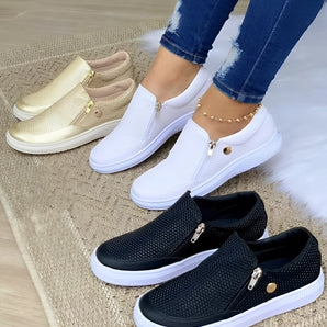 
A pair of women's slip-on sneakers with a breathable mesh upper, featuring a lightweight design and a convenient zipper closure. The sneakers are predominantly white with black and blue accents, suitable for casual wear. They are shown being worn with jeans, emphasizing their use as a comfortable walking shoe.