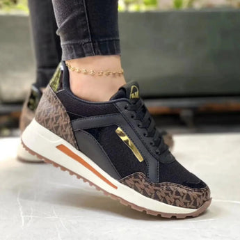 Grey women's sneakers with gold accents, trendy casual chic design. Displayed with a plant in the background, highlighting their sporty and fashionable appearance.
