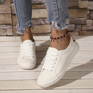 Women's stylish white lace-up sneakers, comfortable low-top trainers, displayed on a model wearing a grey dress. White sneakers with black accents.
