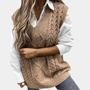 Women's tan cable knit sweater vest with a sleeveless design and a V-neck, shown on a person wearing a grey dress shirt underneath.