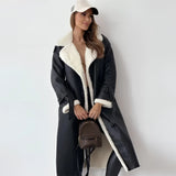 Woman wearing a tan double-breasted shearling trench coat with a black hat, showcasing the coat's length, sleeves, and waist detailing.