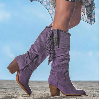 Tan suede mid-calf boots with fringe detailing, shown in a western boho style, featuring a purple background.