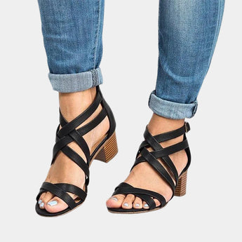 Women's black chunky heel sandals with strappy design and buckle strap, shown on a model wearing jeans.