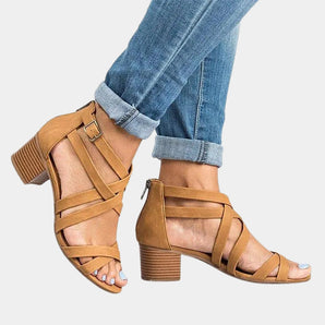 Tan leather strappy chunky heel sandals with a buckle strap on a woman's foot, paired with denim jeans.