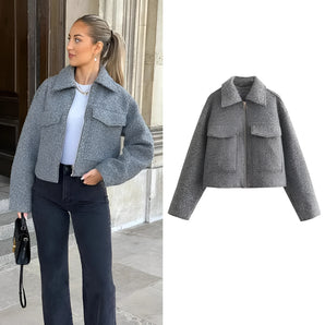 A women's trendy grey wool cropped trucker jacket with a collar and long sleeves, designed as winter outerwear. The jacket is featured without any additional clothing or accessories, emphasizing its stylish and fashionable appearance.