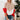 
A woman wearing an oversized beige tri-color sweater paired with jeans, standing in a well-lit room with a decorative flowerpot in the background, showcasing cozy fall knitwear fashion.