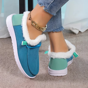 Women's turquoise fur-lined slip-on shoes paired with denim jeans, highlighting stylish winter footwear on a person's legs.