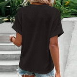 A woman wearing a white short sleeve V-neck blouse with a geometric pattern, paired with jeans, standing outdoors.