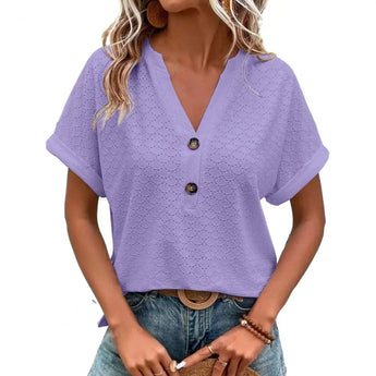 Woman wearing a purple V-neck textured blouse with short sleeves and geometric patterns, paired with jeans.
