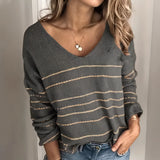 A woman wearing a gray v-neck sweater with white stripes, designed for fall fashion. The sweater is styled for a chic look, paired with jeans, highlighting its versatile and casual appeal.