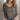 A woman wearing a gray v-neck sweater with white stripes, designed for fall fashion. The sweater is styled for a chic look, paired with jeans, highlighting its versatile and casual appeal.