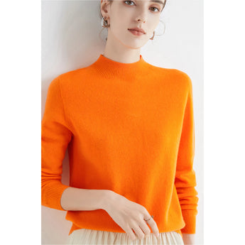 A woman wearing a vibrant orange cashmere turtleneck sweater, showcasing the premium knitwear with long sleeves and a snug collar, styled in a relaxed fit covering the waist, in size 2XL.