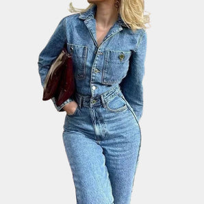 
A women's vintage denim jumpsuit featuring a fitted design with long sleeves and pockets, shown in a greyish tone. The jumpsuit has a classic style, emphasizing the waist, and is suitable for casual or semi-formal wear.
