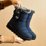 Women's waterproof insulated snow boots in electric blue, featuring a non-slip sole, thermal insulation, and a durable design. The image captures a close-up of a person's lower legs and hands, showcasing the boots' stylish pattern and protective features.