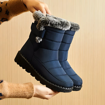 Women's waterproof insulated snow boots in electric blue, featuring a non-slip sole, thermal insulation, and a durable design. The image captures a close-up of a person's lower legs and hands, showcasing the boots' stylish pattern and protective features.