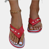 A pair of Women's White Flat Sandals featuring a rhinestone ankle chain, shown on a foot with red nail polish against a red background, highlighting summer fashion style.