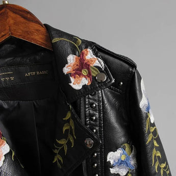 Women's white leather bomber jacket featuring intricate floral embroidery, with details including a stylish collar and long sleeves. The jacket has a Spring Moto design, blending fashion with functional embellishments.