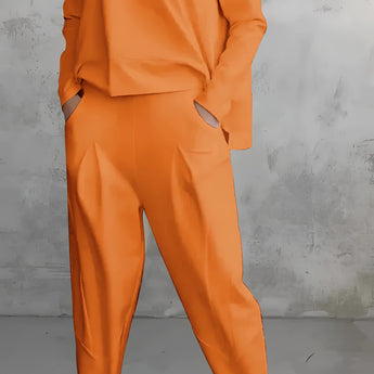 
A woman wearing an orange 3XL lounge set consisting of a minimalist sweatshirt and relaxed joggers. The top features long sleeves and a simple collar, while the bottom has a comfortable waist and fits loosely around the thighs.