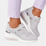 
A pair of women's platform sneakers featuring a stylish design with a white and gray color scheme and a side zipper, shown worn on a foot paired with casual clothing.