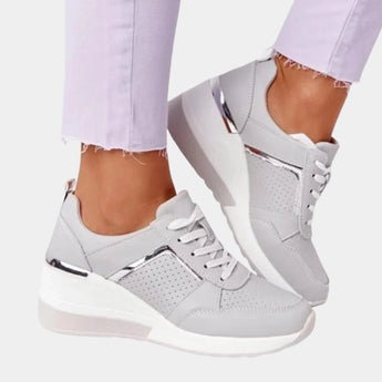
A pair of women's platform sneakers featuring a stylish design with a white and gray color scheme and a side zipper, shown worn on a foot paired with casual clothing.