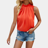 
A woman wearing a white pleated high neck blouse paired with distressed denim shorts. Her arms are relaxed at her sides, highlighting the long sleeves and fitted waist of the blouse.