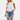Women's white pleated high neck blouse paired with distressed denim shorts; the outfit showcases a stylish and casual look, highlighting the blouse's elegant design and the shorts' trendy appearance.