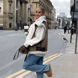 Woman wearing a white shearling vest standing outdoors in an urban setting.